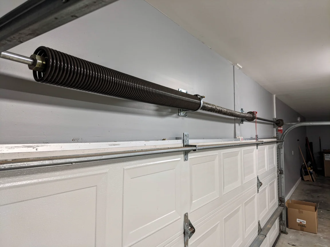 A garage door torsion spring is mounted above a white garage door.